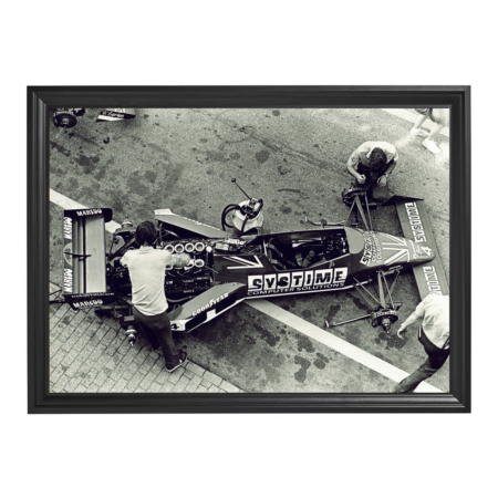 Framed black-and-white photo of mechanics working on a vintage Formula race car in pit lane.